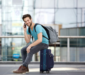 young man sitting by suitcase talking to someone on phone