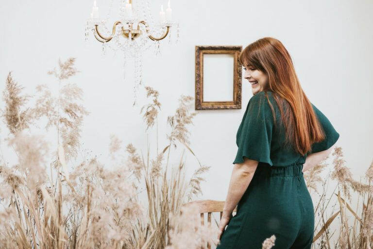 A cheerful plus size woman wearing a green overalls surrounded by tall grass